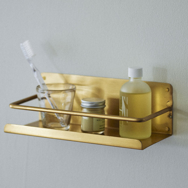 Gold wall-mounted shelf with bathroom products on a light gray background
